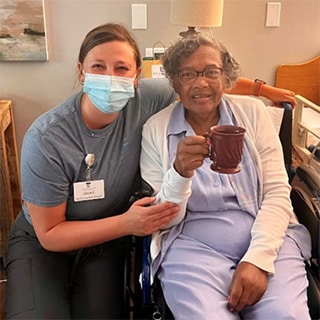Woman in wheelchair holding coffee mug and sitting next to caregiver