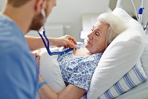 Caregiver using stethoscope on woman in hospital bed